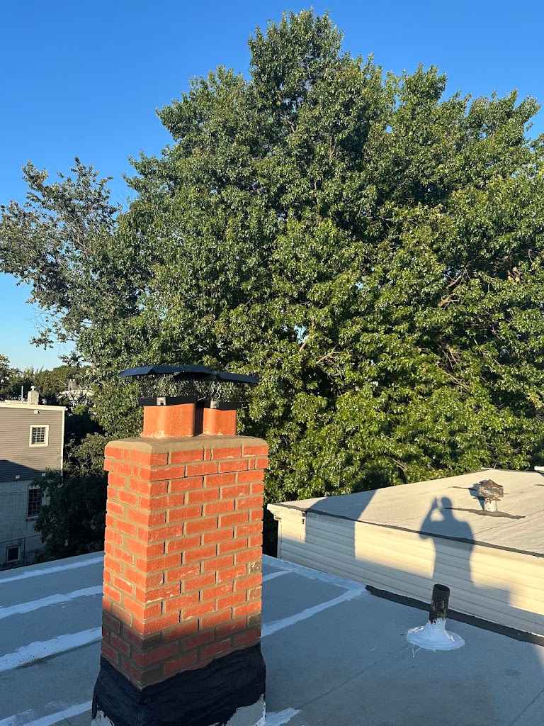 Brick chimney with a black metal chimney cap rising from a flat roof