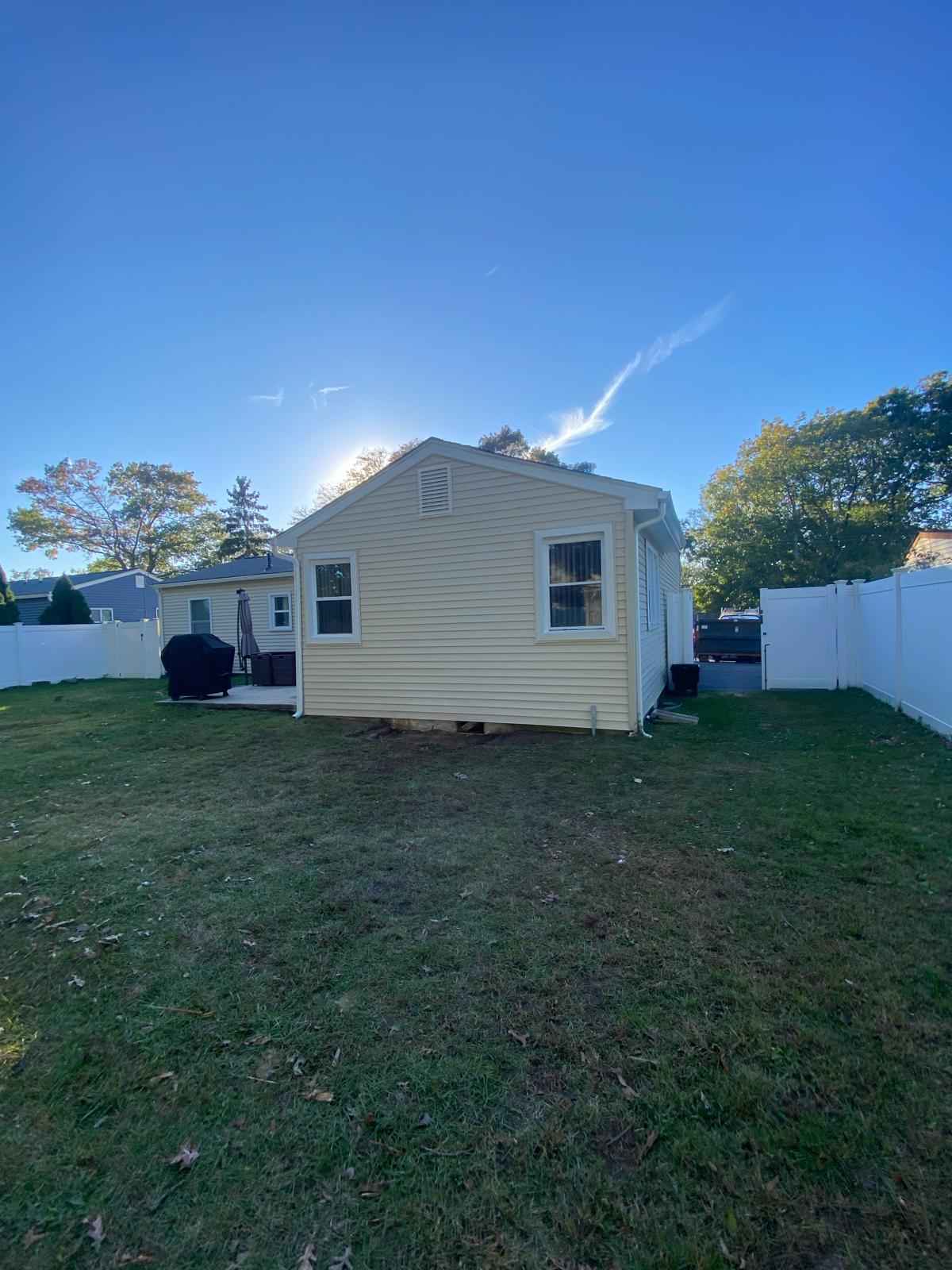 The same gable wall finished in new tan siding with no chimney, seen from the backyard