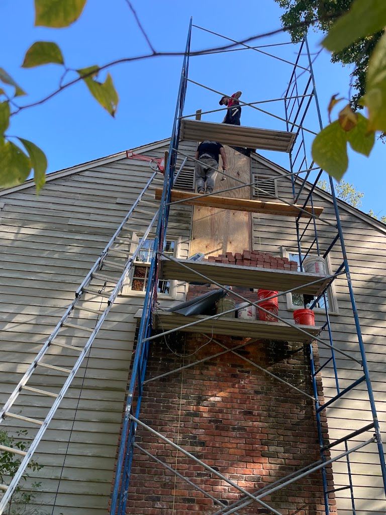 Scaffolding built up the side of a house around a tall brick chimney, with masons working at the top