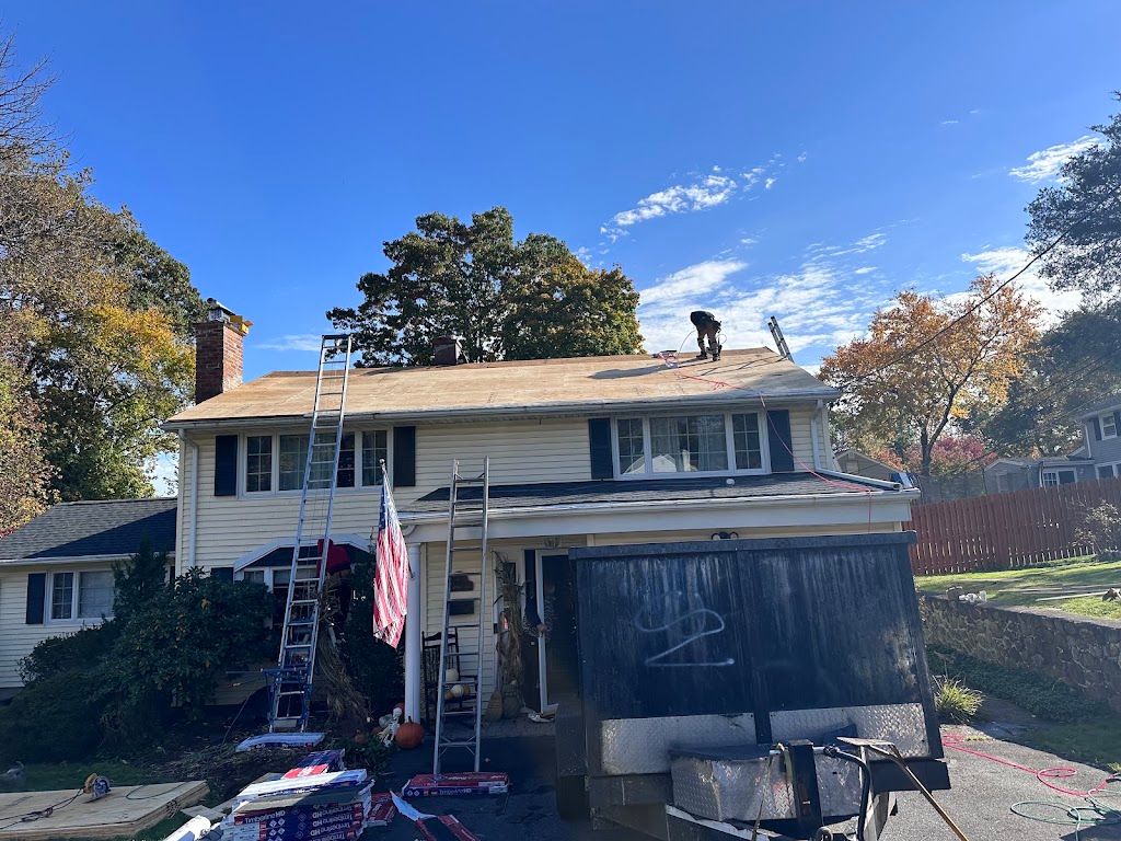 Roofers working on a colonial home with ladders set against the front of the house