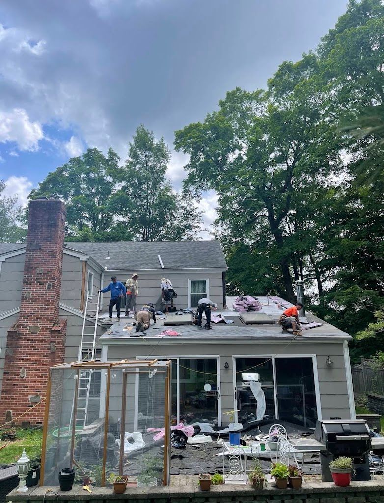 Crew shingling a roof section beside a tall brick chimney