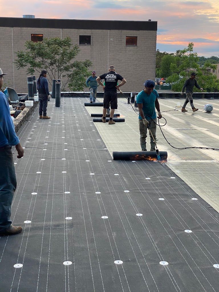 Crew torching down modified bitumen roll roofing on a large flat roof